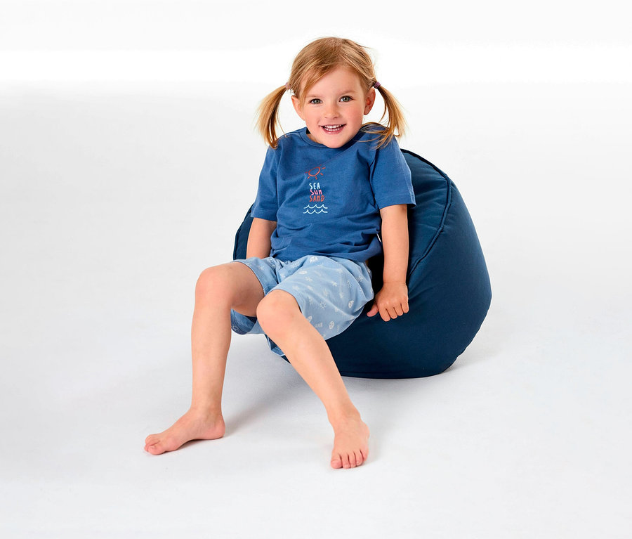 Une fille est assise sur un pouf et porte un pyjama court pour enfant SCHIESSER.