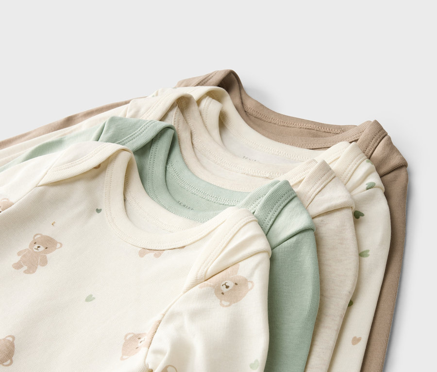 Pile de bodies pour bébé beiges, verts et blancs avec motifs d'ours et de cœurs.