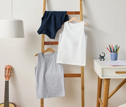 Une échelle supporte des débardeurs gris, blancs et bleus. Une guitare se trouve à côté de l'échelle et un bureau à côté.
