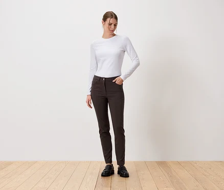 Une femme se tient debout, une main dans la poche de son pantalon, devant un mur blanc.