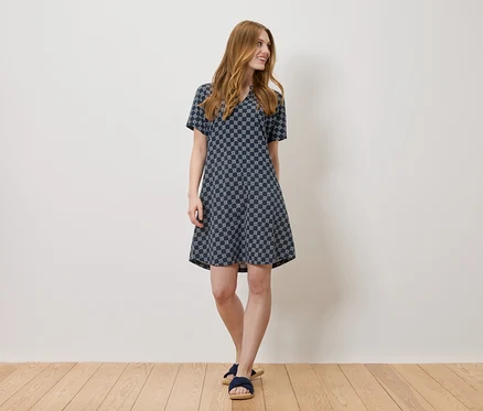 Une femme se tient devant un mur blanc et porte une robe bleue à motifs.