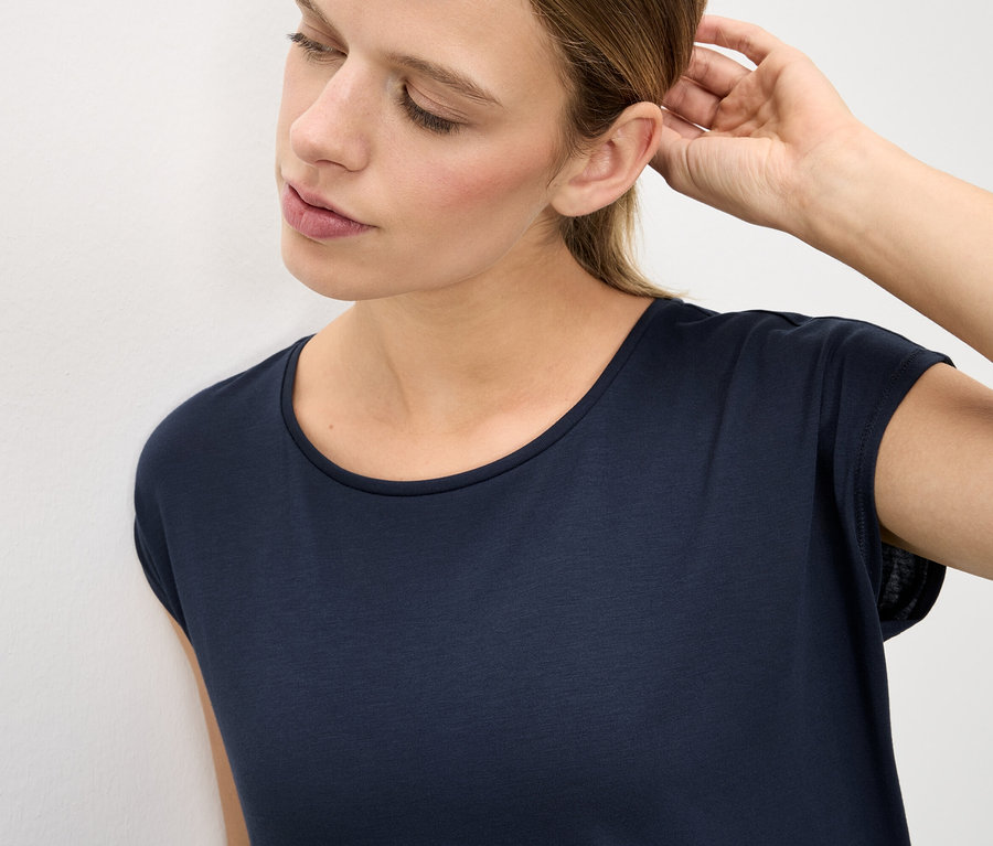 Femme touchant son oreille portant un t-shirt foncé.