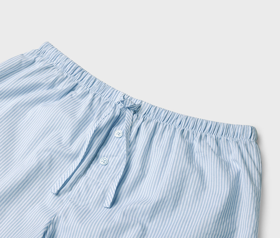 Gros plan sur un pantalon de pyjama rayé bleu clair et blanc avec une taille élastique et une patte de boutonnage.
