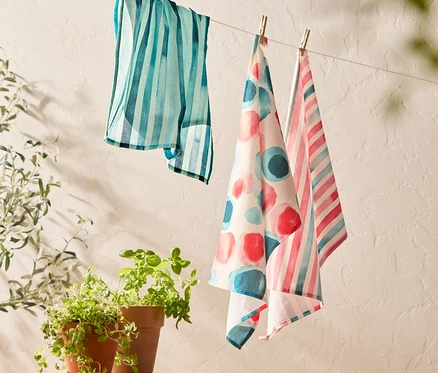 Trois torchons suspendus à une corde à linge à côté d'un tabouret en bois avec deux plantes en pot.