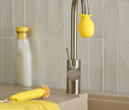 Un évier avec un robinet auquel est fixée une éponge jaune, à côté d'une brosse jaune et d'une bouteille.