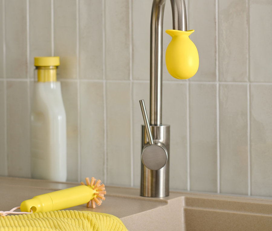Un évier avec un robinet auquel est fixée une éponge jaune, à côté d'une brosse jaune et d'une bouteille.