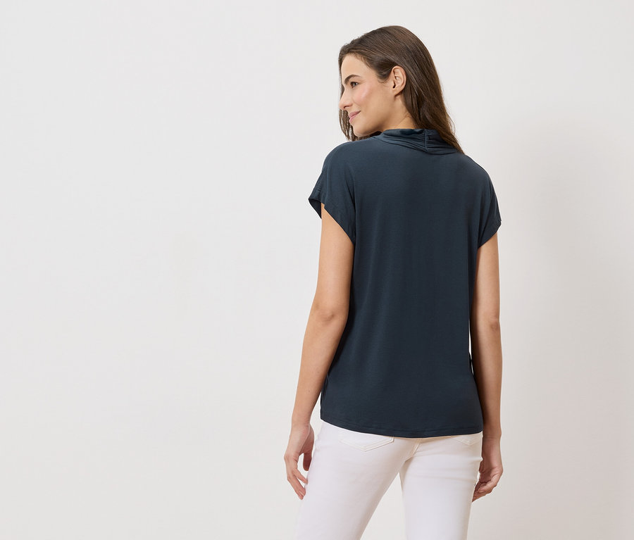 Vue arrière d'une femme aux longs cheveux bruns portant un haut bleu marine et un jean blanc.