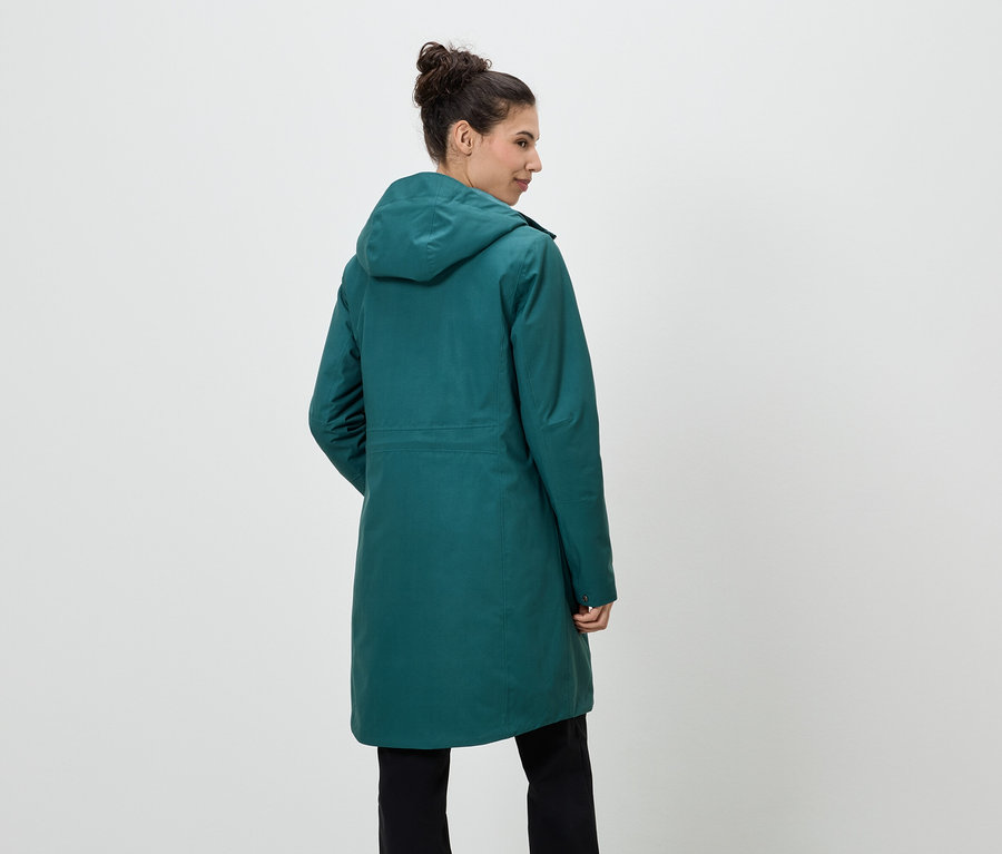 Vue arrière d'une femme portant un chignon, un manteau vert émeraude et un pantalon noir.