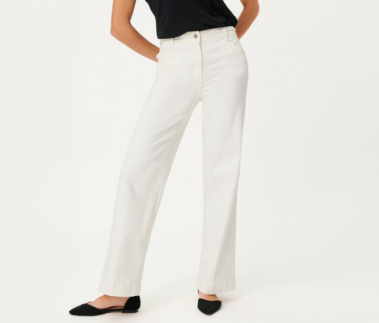 Une femme porte un jean Olsen à jambes larges et des chaussures noires sur fond blanc.