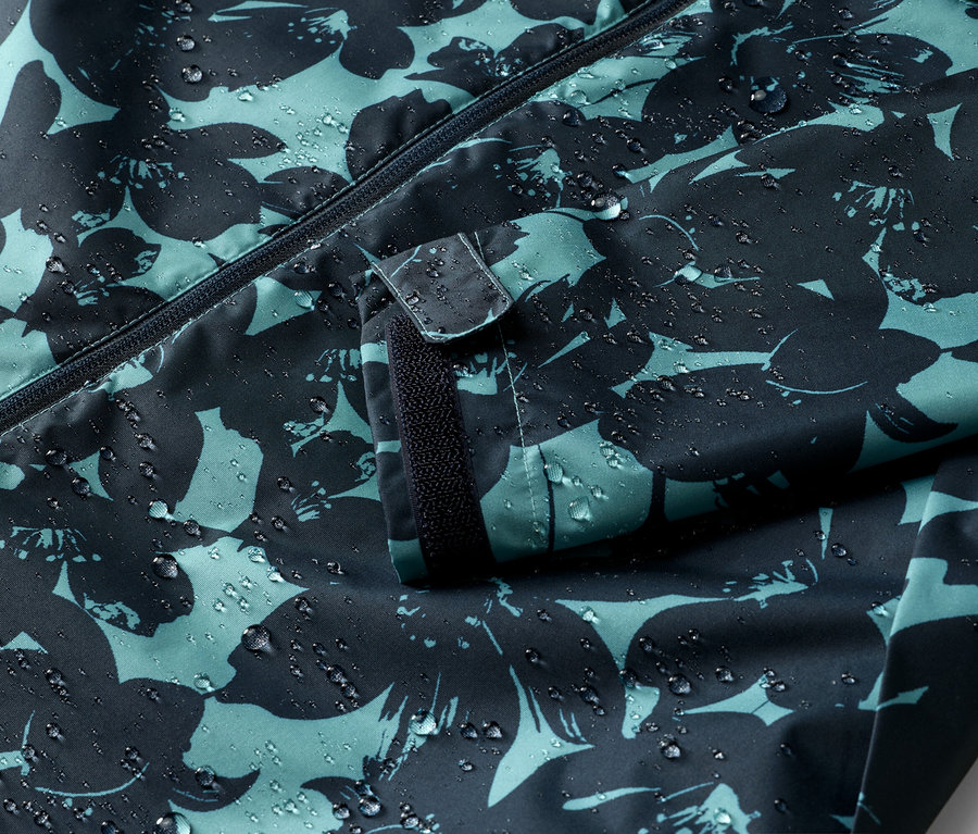 Gros plan d'une veste imperméable avec fermeture éclair et motif floral, sur laquelle on peut voir des gouttes d'eau.
