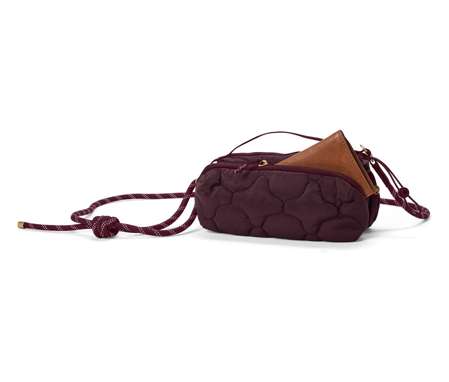 Un sac à main bordeaux matelassé avec un portefeuille marron à l'intérieur et une épaisse bandoulière en corde repose sur un fond blanc.