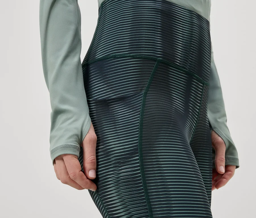 Gros plan d'une personne portant des leggings à rayures horizontales et un haut à manches longues vert.