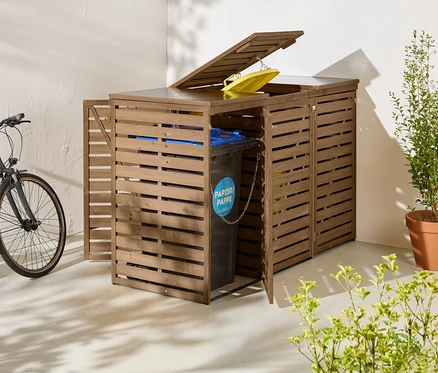 Trois abris poubelles marron sont placés à l'extérieur, l'un d'eux ayant une porte ouverte et une poubelle. À côté, un vélo et une plante en pot.