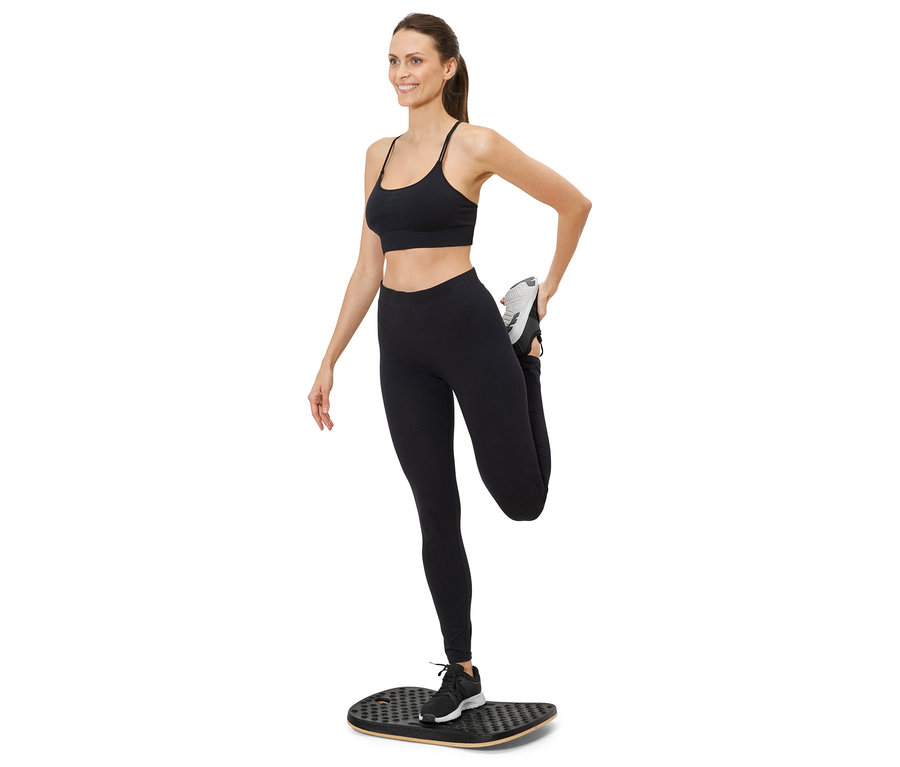 Femme étire sa jambe sur une planche d'équilibre, portant des vêtements de sport.