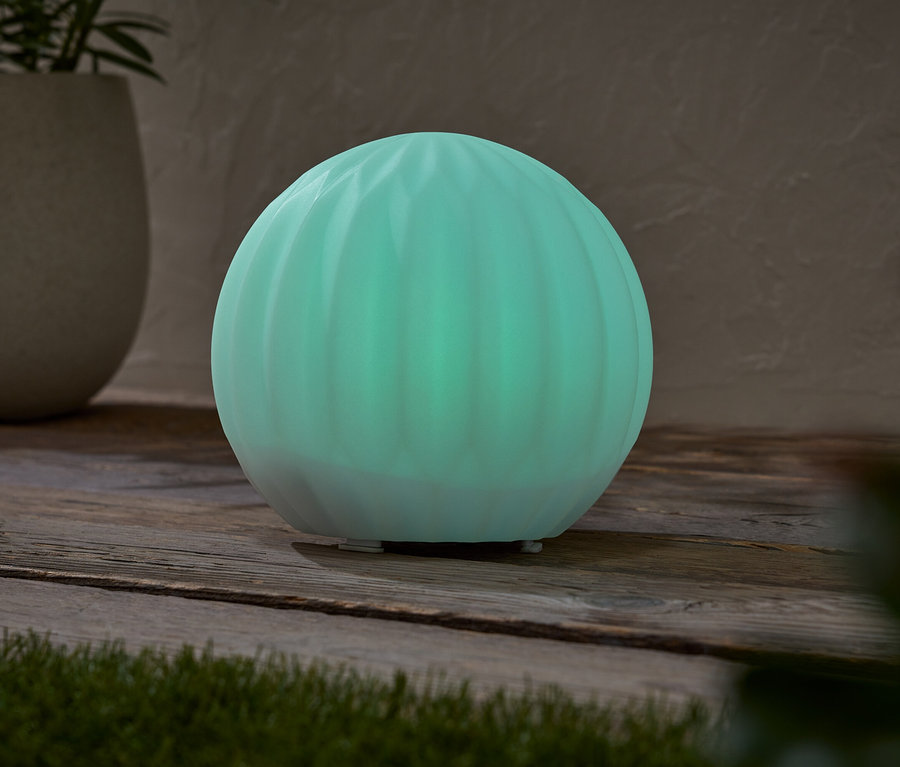 Une lampe sphérique turquoise lumineuse est posée sur une table en bois, à côté d'un pot contenant une plante.