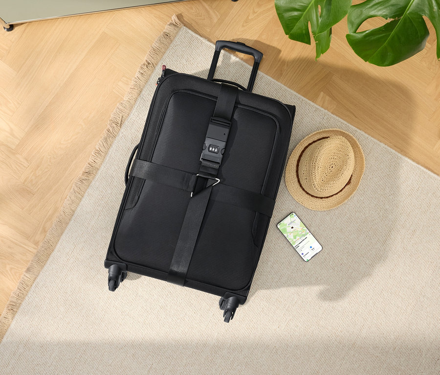 Valise noire à roulettes avec chapeau et smartphone sur un tapis beige.