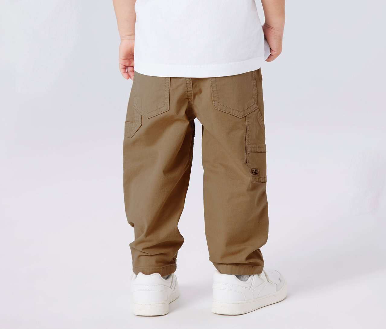 Gros plan du dos d'un enfant portant un pantalon en sergé pour enfant NAME IT et des baskets blanches.