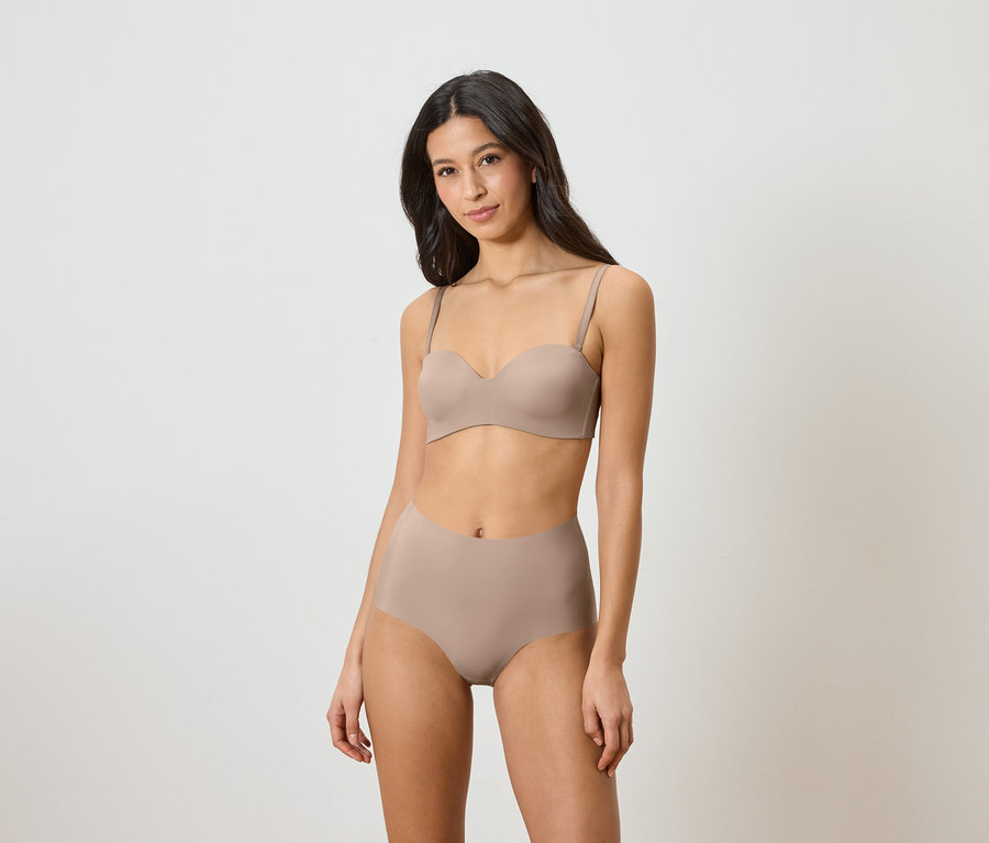 Femme portant un soutien-gorge bandeau et une culotte taille haute beige.