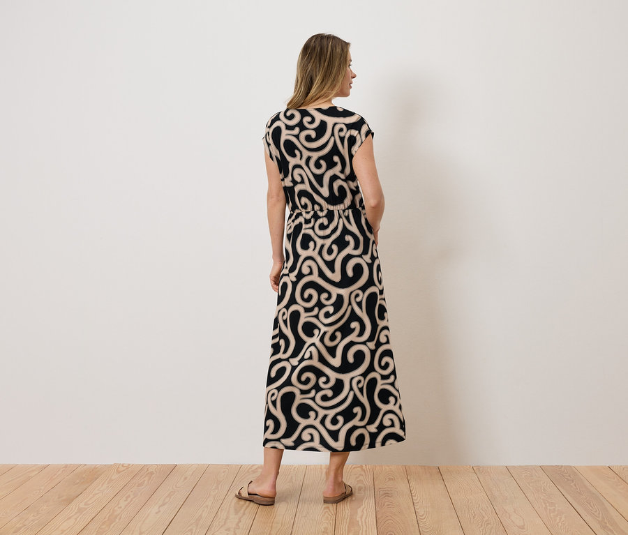 Une femme se tient dos à la caméra et porte une robe maxi noire avec des volutes beiges.