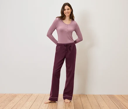 Une femme portant un haut mauve à manches longues et un pantalon bordeaux à cordon de serrage, debout sur un plancher en bois.