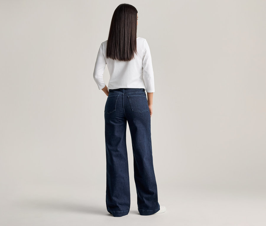 Vue de dos d'une femme aux longs cheveux foncés, portant un chemisier blanc et un jean ample bleu foncé.