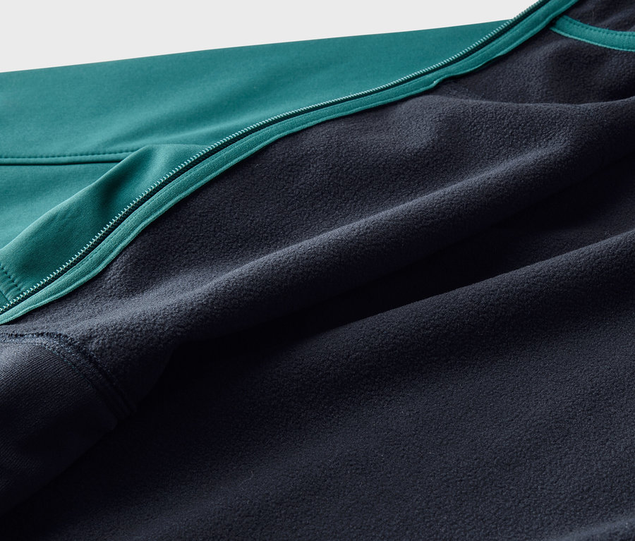 Gros plan d'une veste avec un extérieur lisse turquoise et une doublure en polaire bleu foncé, séparés par une fermeture éclair turquoise.