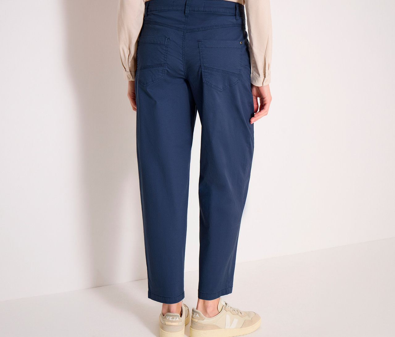 Une personne de dos, portant le pantalon barrel CECIL « Scarlett » bleu, une chemise claire et des baskets claires.