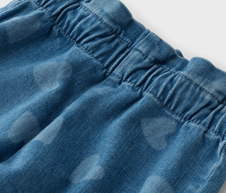 Gros plan sur un jean bleu avec une taille élastique et un motif discret en forme de cœur.