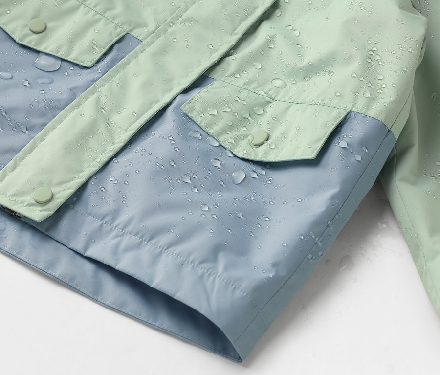 Gros plan d'une veste imperméable bleue et vert menthe avec des gouttes d'eau.