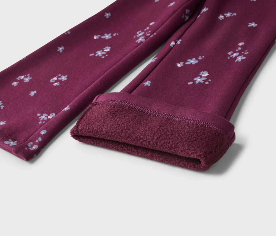 Une paire de leggings rouge foncé avec un petit motif floral bleu clair et blanc. Une jambe est repliée pour révéler une doublure en polaire épaisse, douce et rouge foncé.