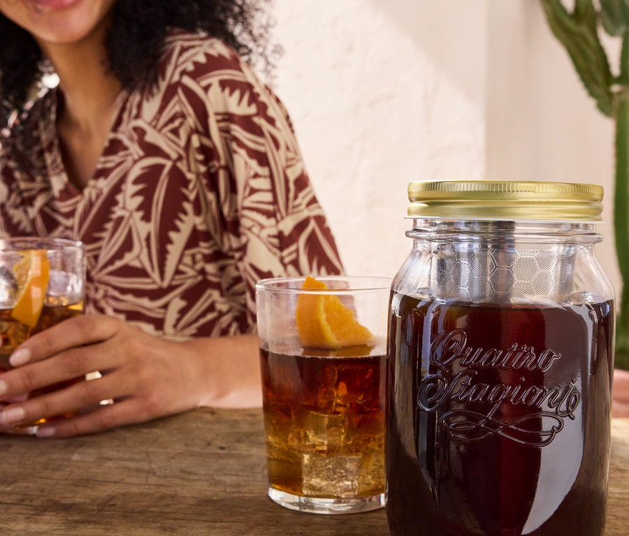 Femme tenant un verre avec une boisson à côté du bocal pour infuser le café à froid « BrewJar » et d'une robe en jersey imprimée.