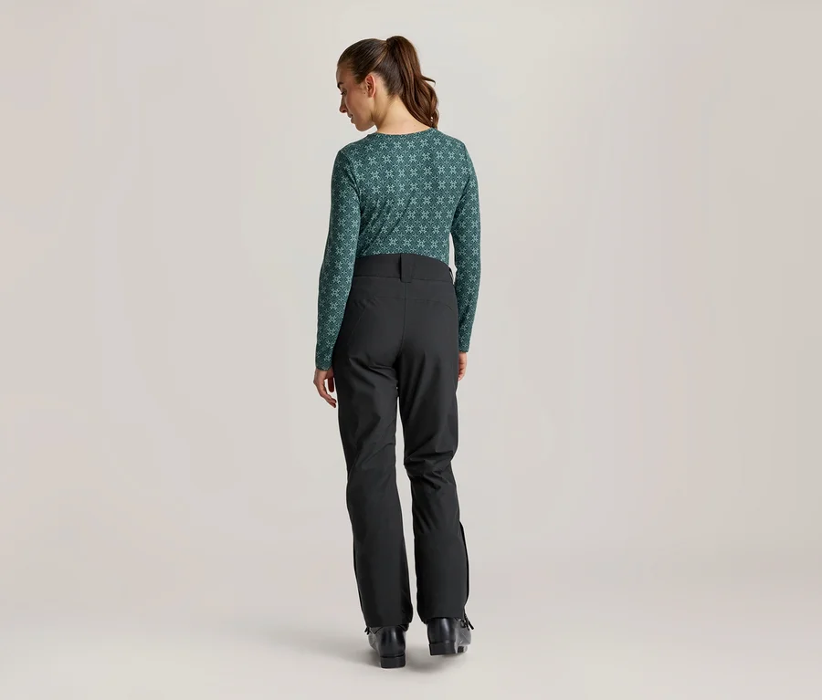 Femme de dos portant un haut à manches longues à motifs et un pantalon de ski noir, la tête légèrement tournée vers la droite.
