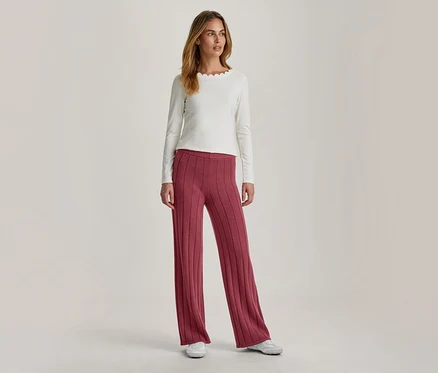 Femme portant un haut écru à manches longues avec un col festonné et un pantalon large côtelé rose foncé, associé à des baskets blanches.