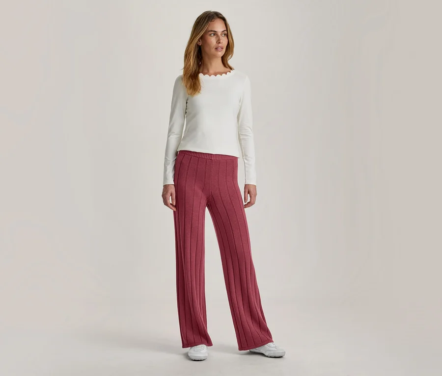 Femme portant un haut écru à manches longues avec un col festonné et un pantalon large côtelé rose foncé, associé à des baskets blanches.