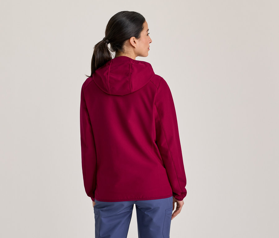 Femme vue de dos, portant une veste à capuche magenta et un pantalon bleu, les cheveux attachés en queue de cheval, regardant vers la droite.