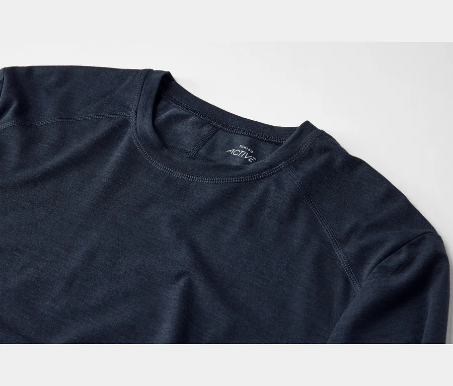 Gros plan d'un t-shirt à manches longues bleu foncé avec un col rond et des coutures visibles, montrant une étiquette blanche « TCHIBO ACTIVE » sur le col intérieur.