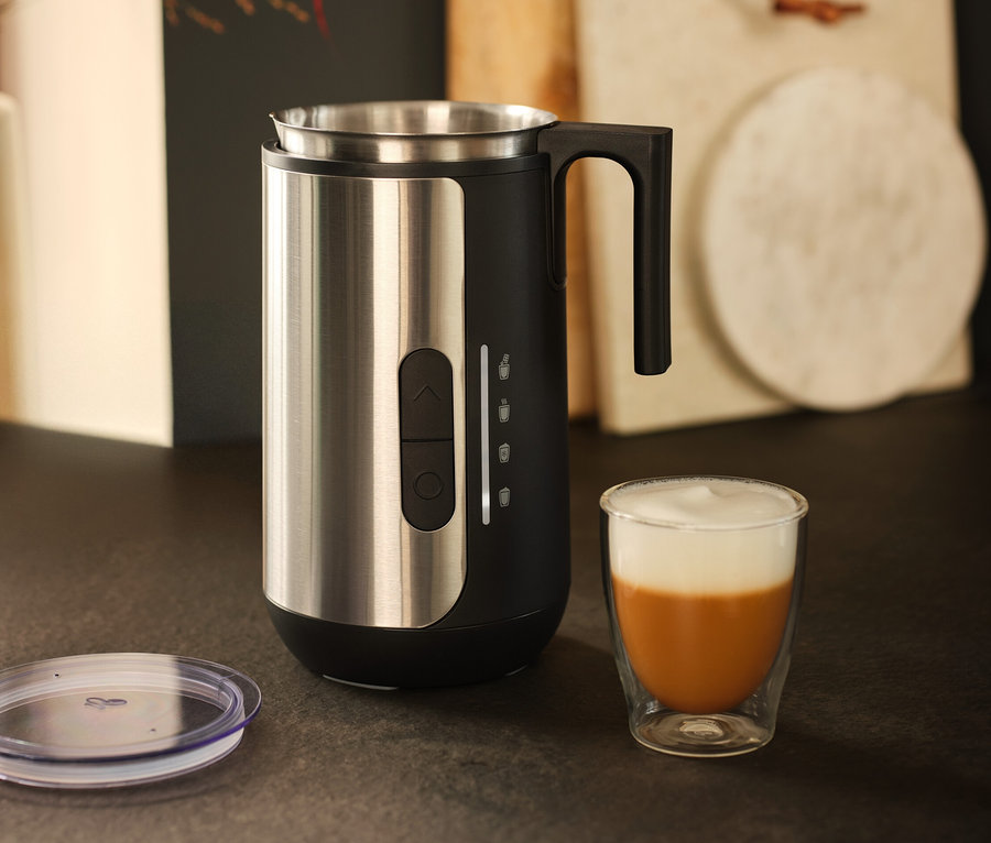 Un mousseur à lait en acier inoxydable est posé à côté d'un verre de café avec de la mousse de lait.