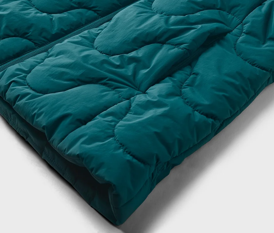 Gros plan d'un tissu matelassé sarcelle avec une fermeture éclair visible sur le côté gauche. Le tissu présente un motif matelassé gonflé et ondulé.