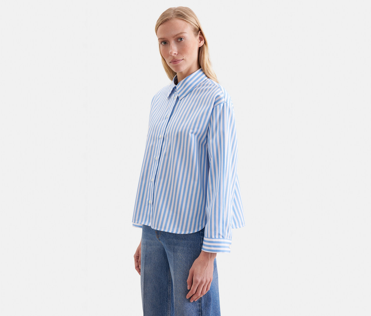 Une femme porte un chemisier oversize Seidensticker bleu et blanc à rayures et un jean bleu.