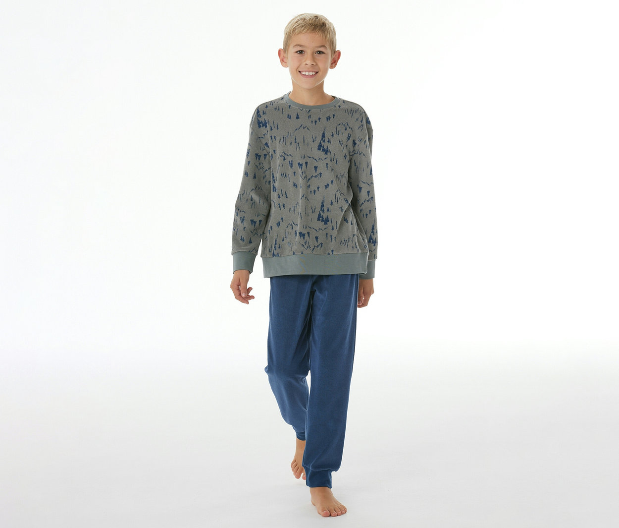 Garçon souriant en pyjama pour enfant SCHIESSER avec bords-côtes: haut gris à motif d'arbres bleus, pantalon bleu. Il est pieds nus.