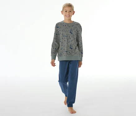 Garçon souriant en pyjama pour enfant SCHIESSER avec bords-côtes: haut gris à motif d'arbres bleus, pantalon bleu. Il est pieds nus.