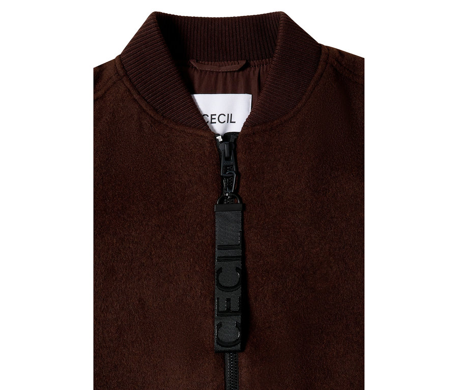 Gros plan d'un blouson CECIL marron avec col côtelé, fermeture éclair et étiquette de marque.