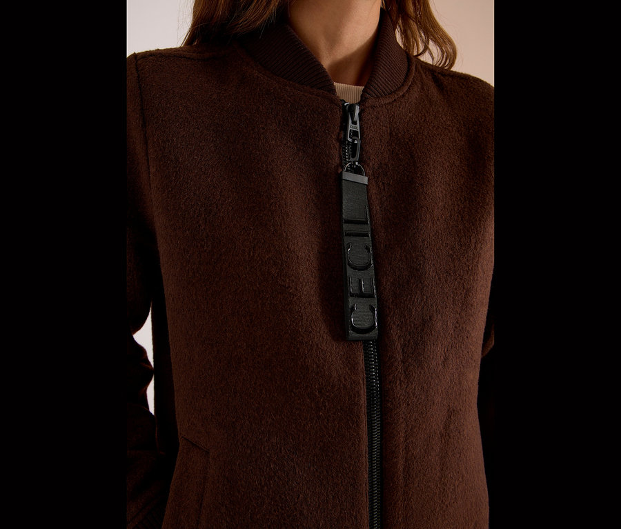 Gros plan d'une personne portant un blouson CECIL marron, avec col côtelé et fermeture éclair avec tirette CECIL.