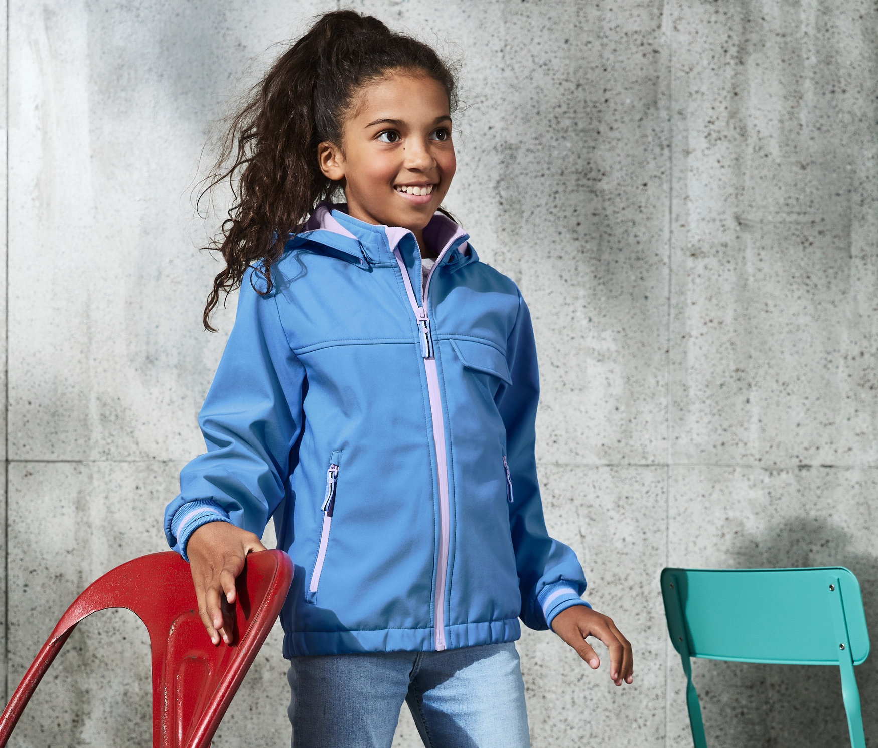 Une fille porte une veste softshell bleue avec des matériaux recyclés et se tient debout.