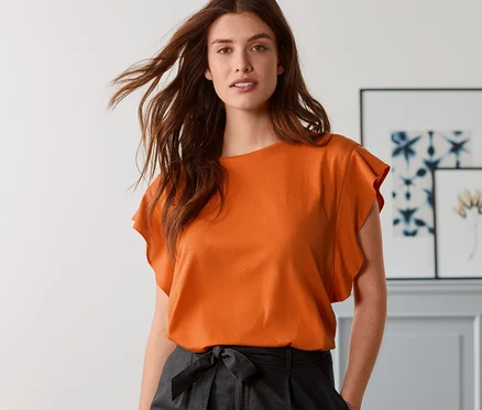 Femme posant en T-shirt à volants orange et short en lin noir.