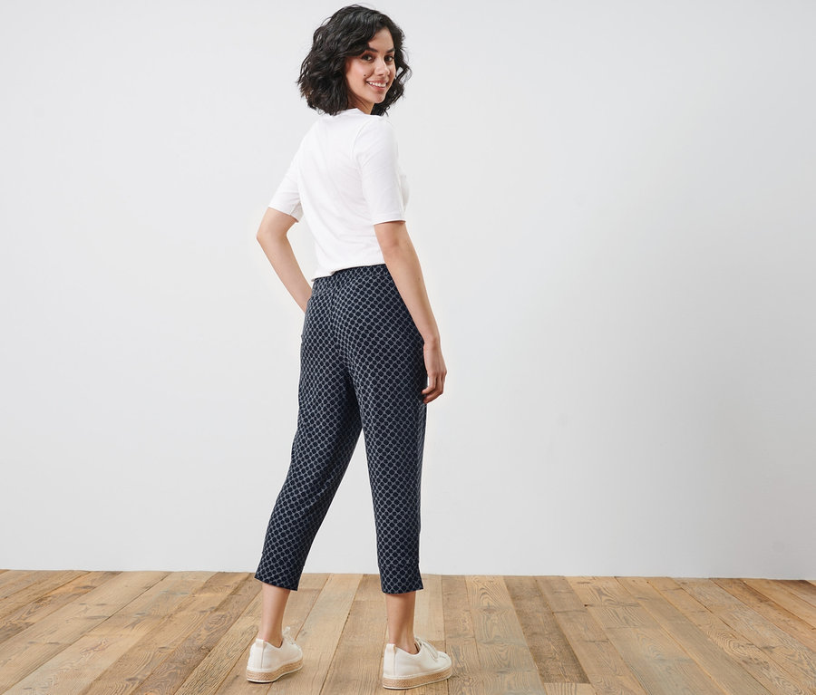 Une femme regardant par-dessus son épaule pose en pantalon 3/4 en jersey imprimé, t-shirt blanc et baskets.