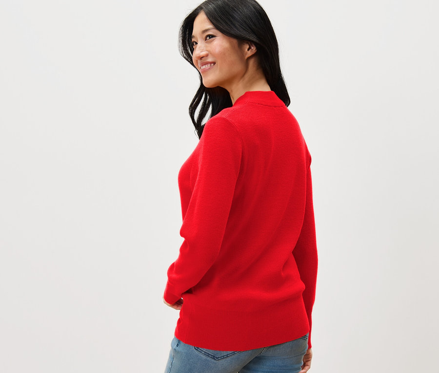 Une femme regarde par-dessus son épaule et porte un pull en maille fine rouge et un jean.