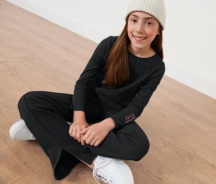 Une fille est assise par terre et porte un t-shirt noir à manches longues pour enfants.