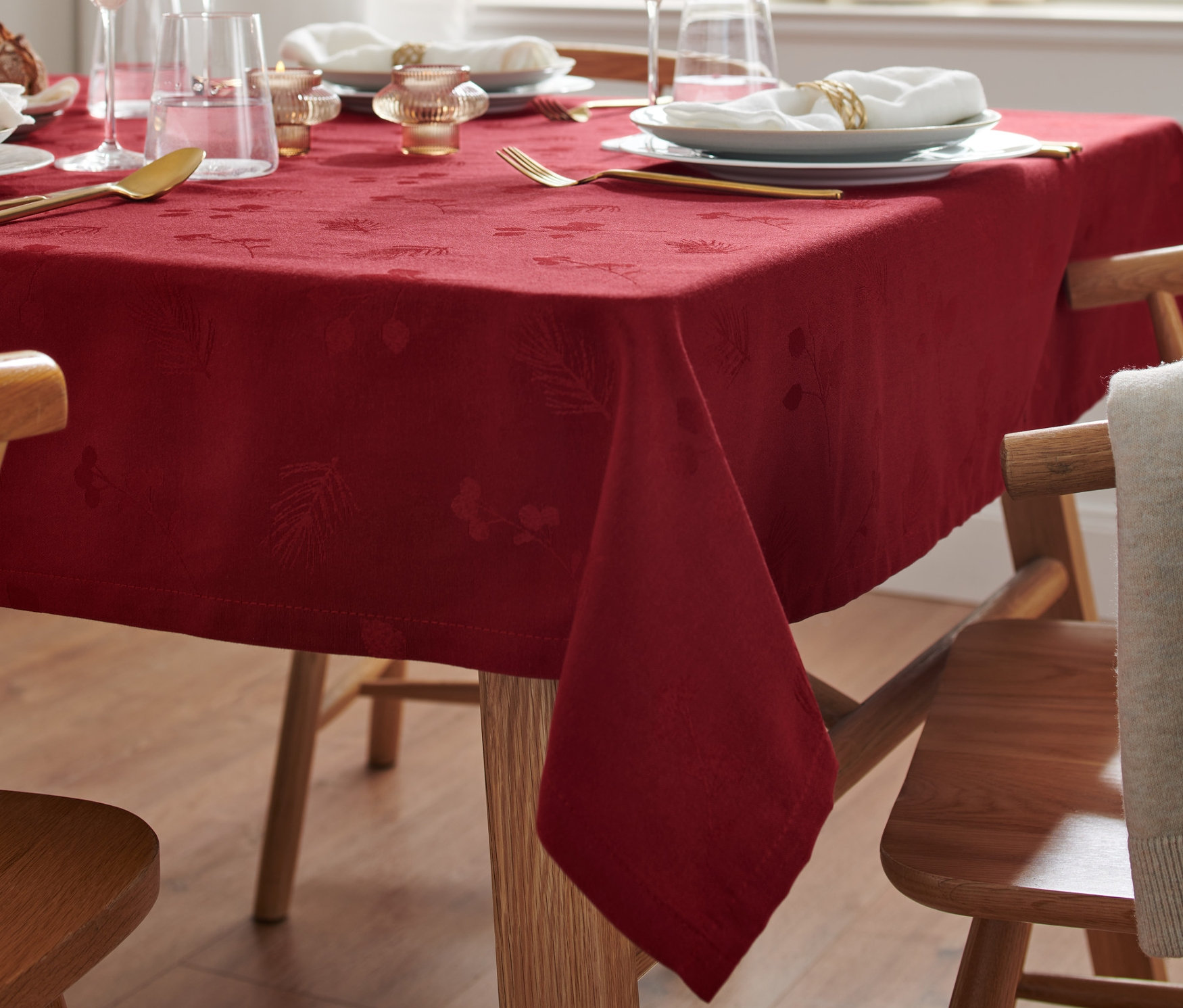 Une nappe jacquard rouge recouvre une table avec des couverts, des verres à vin et des décorations.