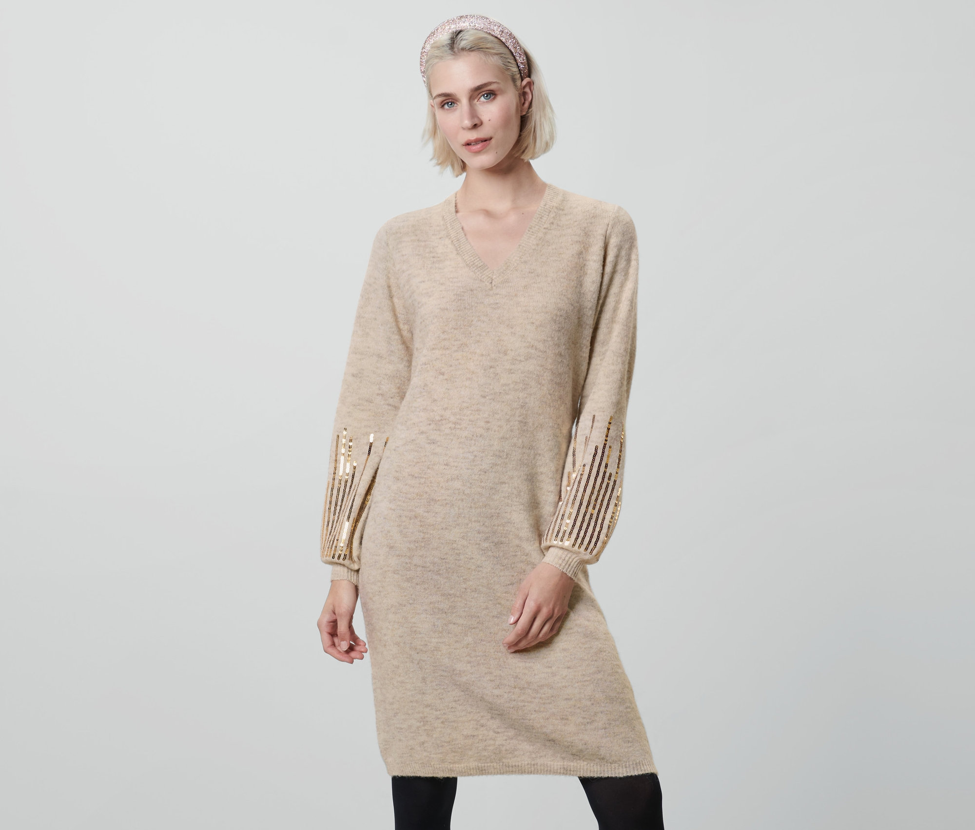 Femme posant en robe en maille beige à paillettes.